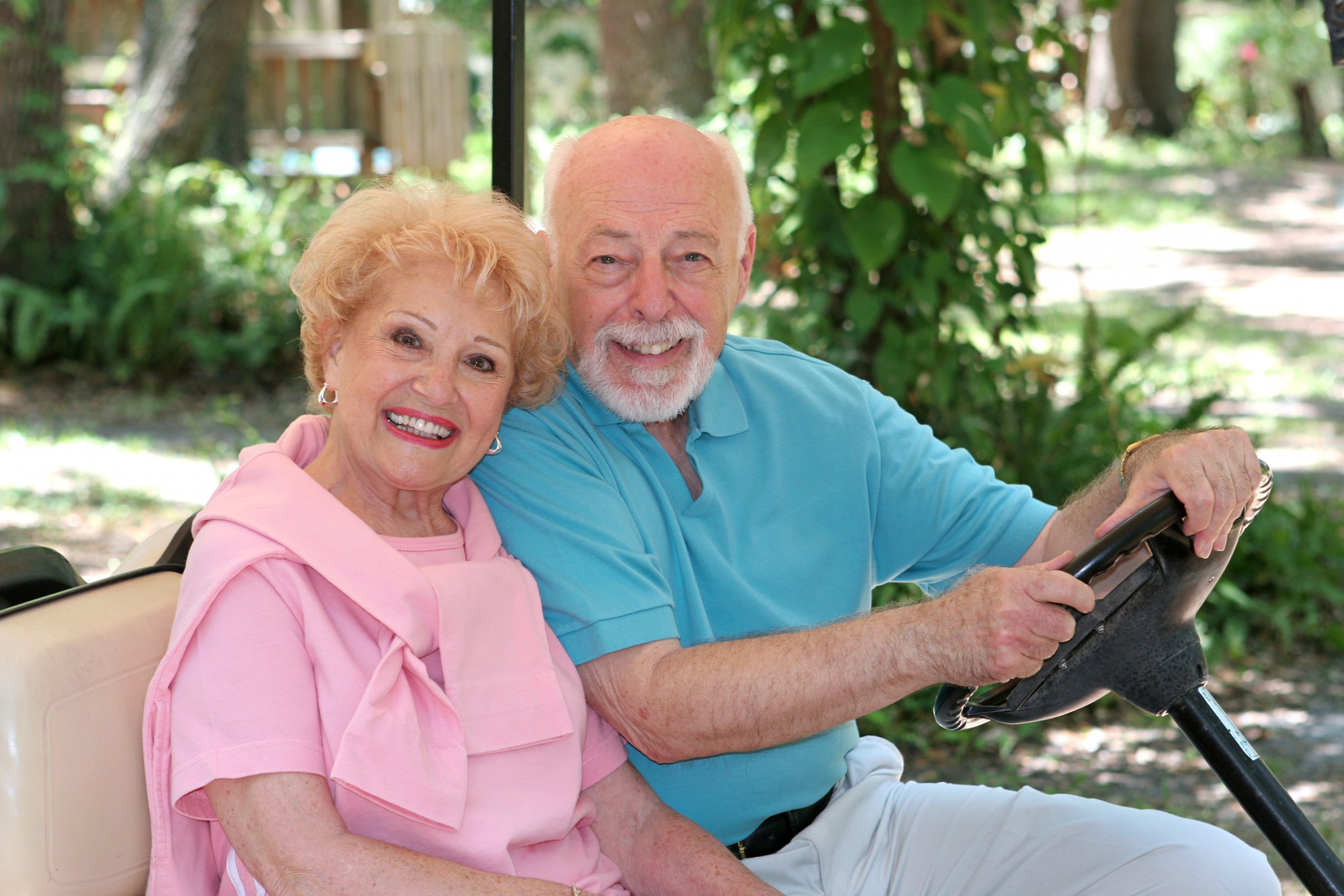 An older couple smiling while riding in a golf cart.