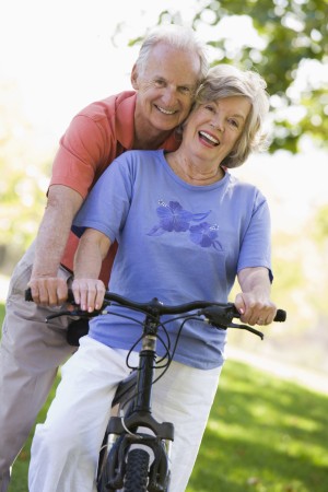 An older couple riding a bicycle in the park.