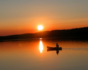 A person in a canoe on a lake at sunset.