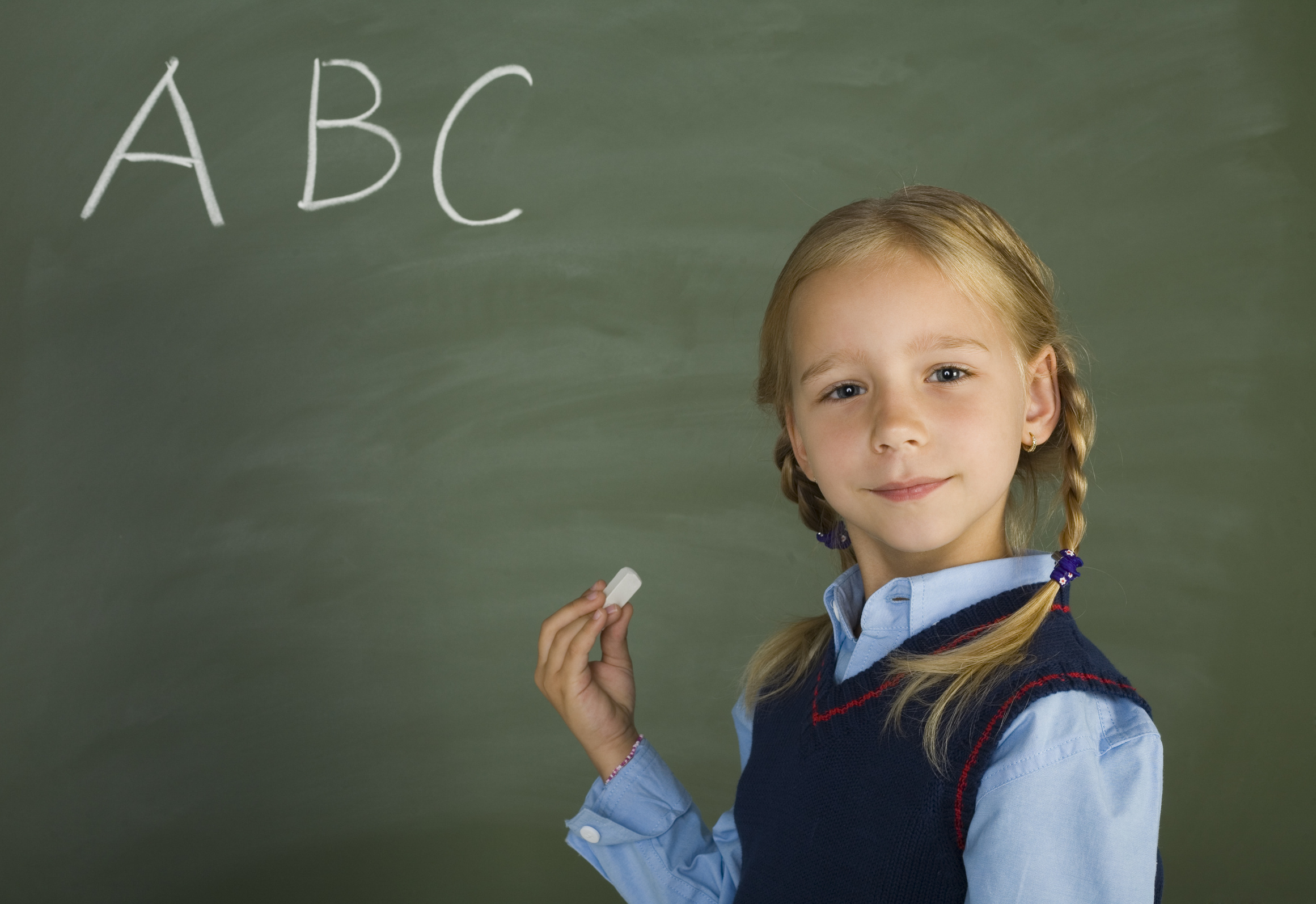 A little girl is standing in front of a blackboard with the letter abc written on it.