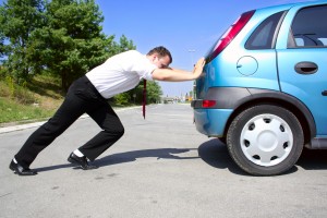 A man pushing a blue car.