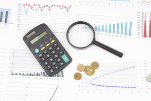 A magnifying glass, calculator, coins and graphs on a white background.