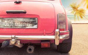 A pink car parked on the beach with palm trees.