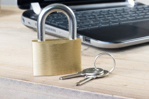 A padlock on a wooden table next to a laptop.