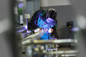 A welder working on a metal pipe in a factory.