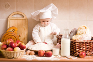 A baby in a chef's hat is making bread.