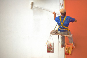 A man on a rope painting a building