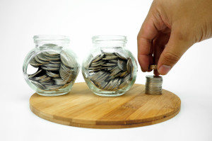 A hand is putting coins into a glass jar.