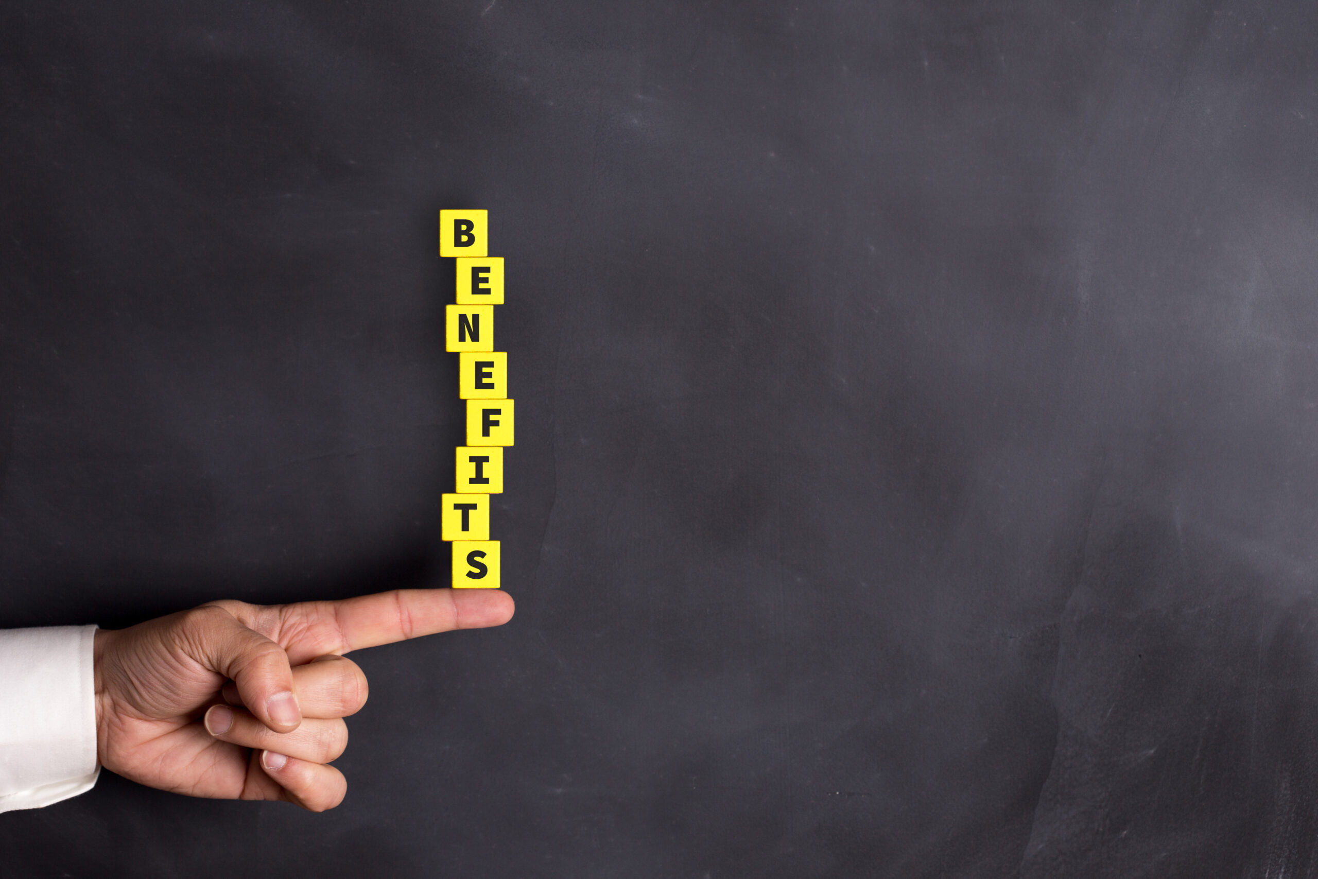 A man is pointing at a chalkboard with the word benefits written on it.