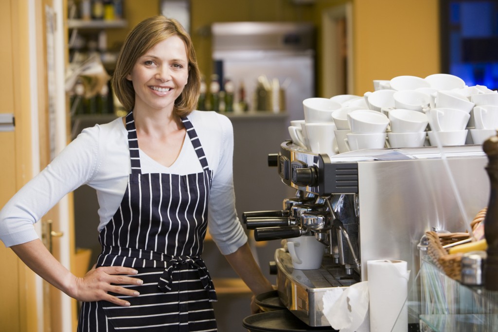 A woman in a striped apron standing in front of a coffee machine.