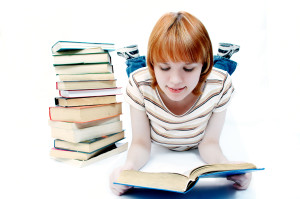 A girl laying on the ground with a stack of books.