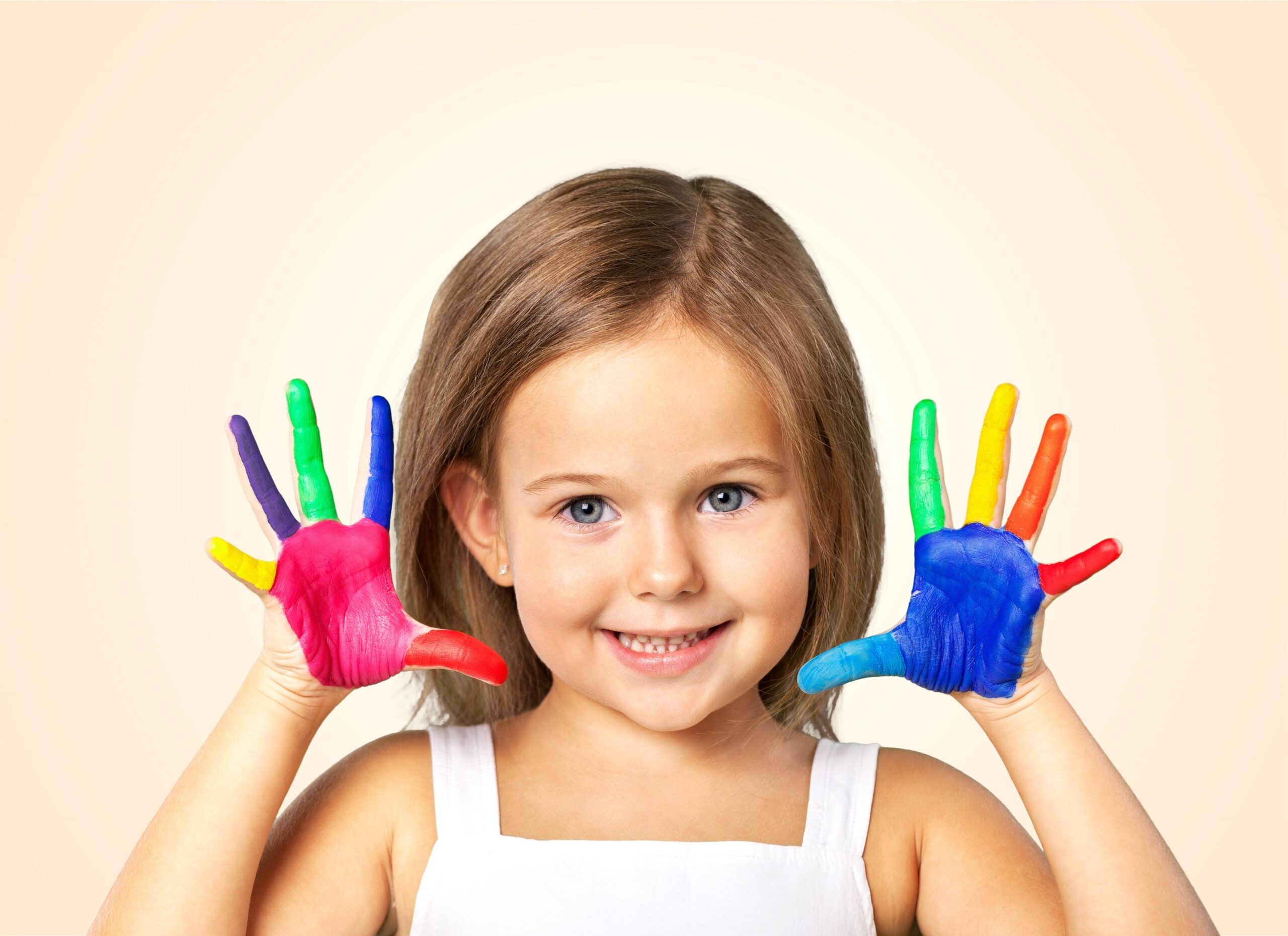 A little girl holding her hands up with colorful paint on them.