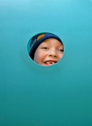 A child is peeking out of a hole in a blue play structure.