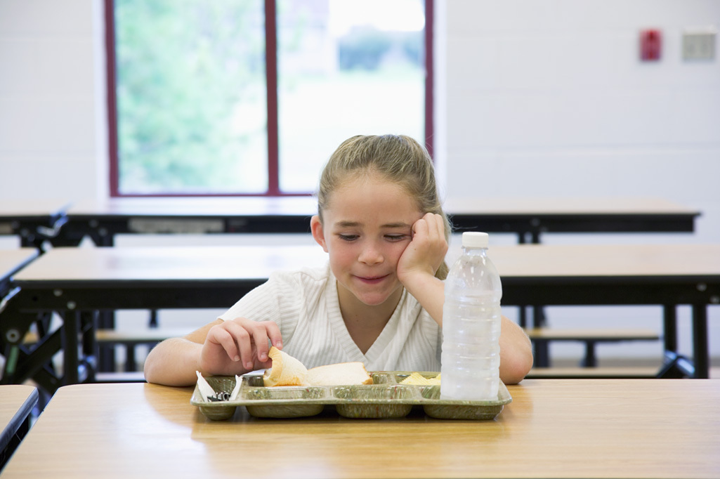 A girl sitting at a table with a tray of food.