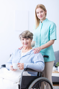 A woman in a wheelchair with a nurse standing next to her.