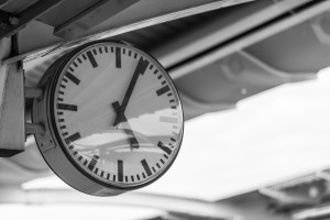 A black and white photo of a clock on a train platform.