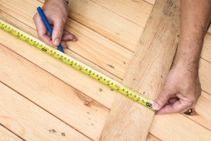 A man measuring a wooden floor with a tape measure.