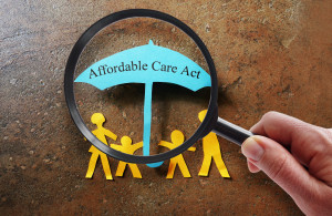 A person holding a magnifying glass looking at a paper with the word affordable care act.