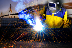 A welder is welding in front of a bridge.