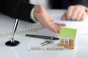 A man is holding a toy house and keys on a desk.