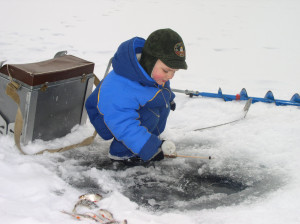 A young boy in a blue jacket is fishing in the snow.