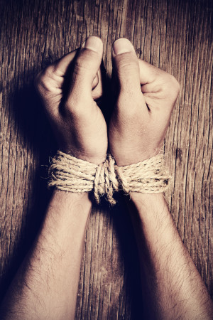 A man's hands tied with rope on a wooden table.