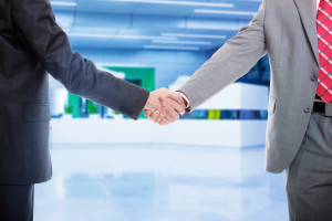 Two businessmen shaking hands in front of an office.