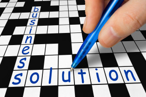 A person writing the word business solution on a crossword puzzle.