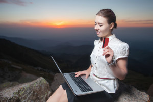 A woman is sitting on top of a mountain with a laptop and credit card.