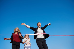 A group of business people running across a red ribbon.