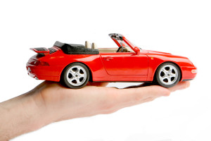 A person holding a red toy car on a white background.