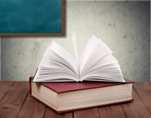 A book on top of a wooden table with a chalkboard behind it.