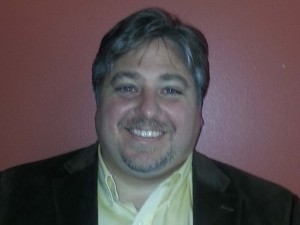 A man smiling in front of a red wall.