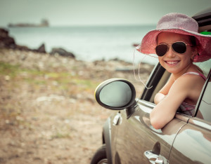 A young girl in a pink hat and sunglasses is sitting in the back seat of a car.