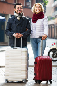 A man and woman standing with suitcases on a city street.