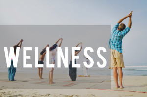 A group of people doing yoga on the beach with the words wellness.