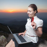 A woman is sitting on top of a mountain with a laptop and credit card.