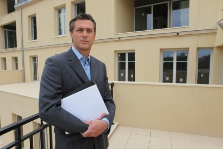 A businessman holding a folder in front of an apartment building.