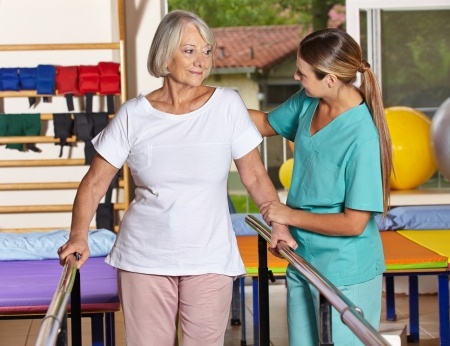 A nurse is helping an older woman in a physical therapy room.