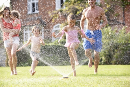 A family playing in the yard with a sprinkler.