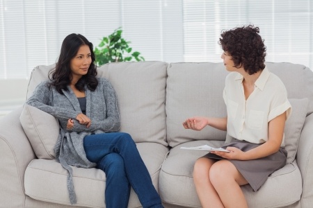 Two women sitting on a couch talking to each other.