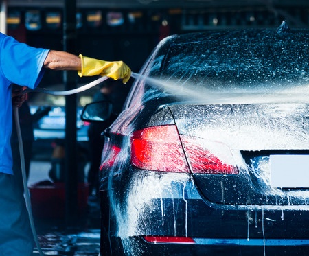 A man is washing a car at a car wash.