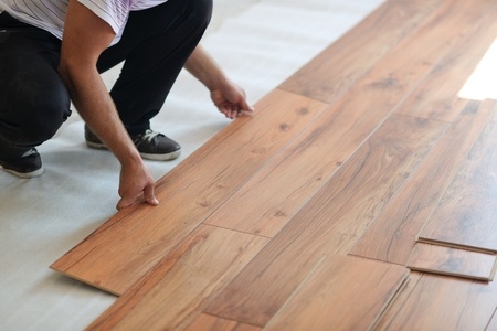 A man is putting down wood flooring in a room.