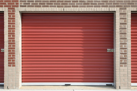 Three red storage doors in a brick building.