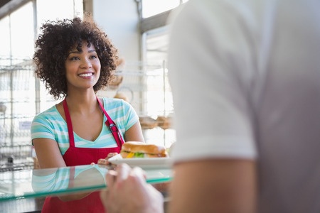 A woman in a red apron is serving a customer in a bakery.