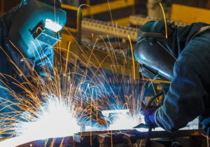 Two welders working in a factory with sparks.