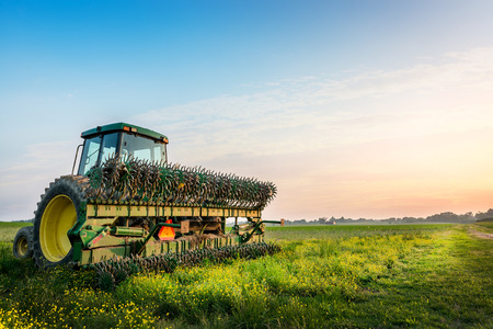 A tractor is working in a field at sunset.