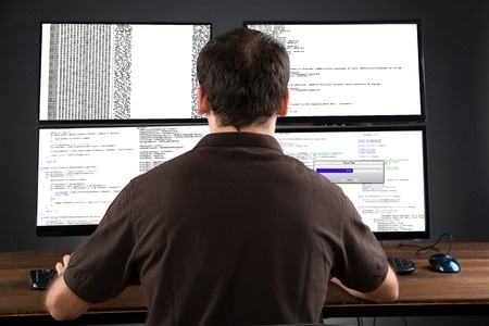 A man sitting at a desk with three monitors.