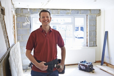 A man in a red shirt standing in an unfinished room.