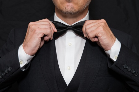 A man in a tuxedo is adjusting his bow tie.